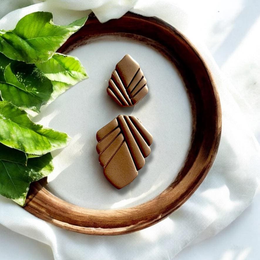 Finished Art Deco-inspired polymer clay earrings displayed in a wooden bowl with leaves for a vintage-inspired look.