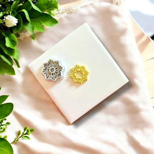Polymer clay seashell wreath charm alongside its matching cutter, displayed on a white tile with fresh leaves.