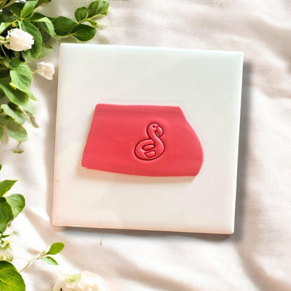 Pink polymer clay impression of flamingo floatie design on white tile with greenery in the background.