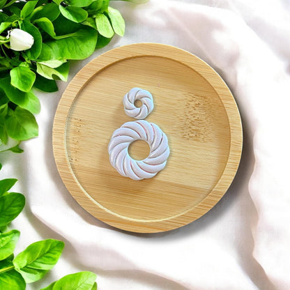 Finished swirl shell earrings on a bamboo tray, with green leaves and white fabric background.