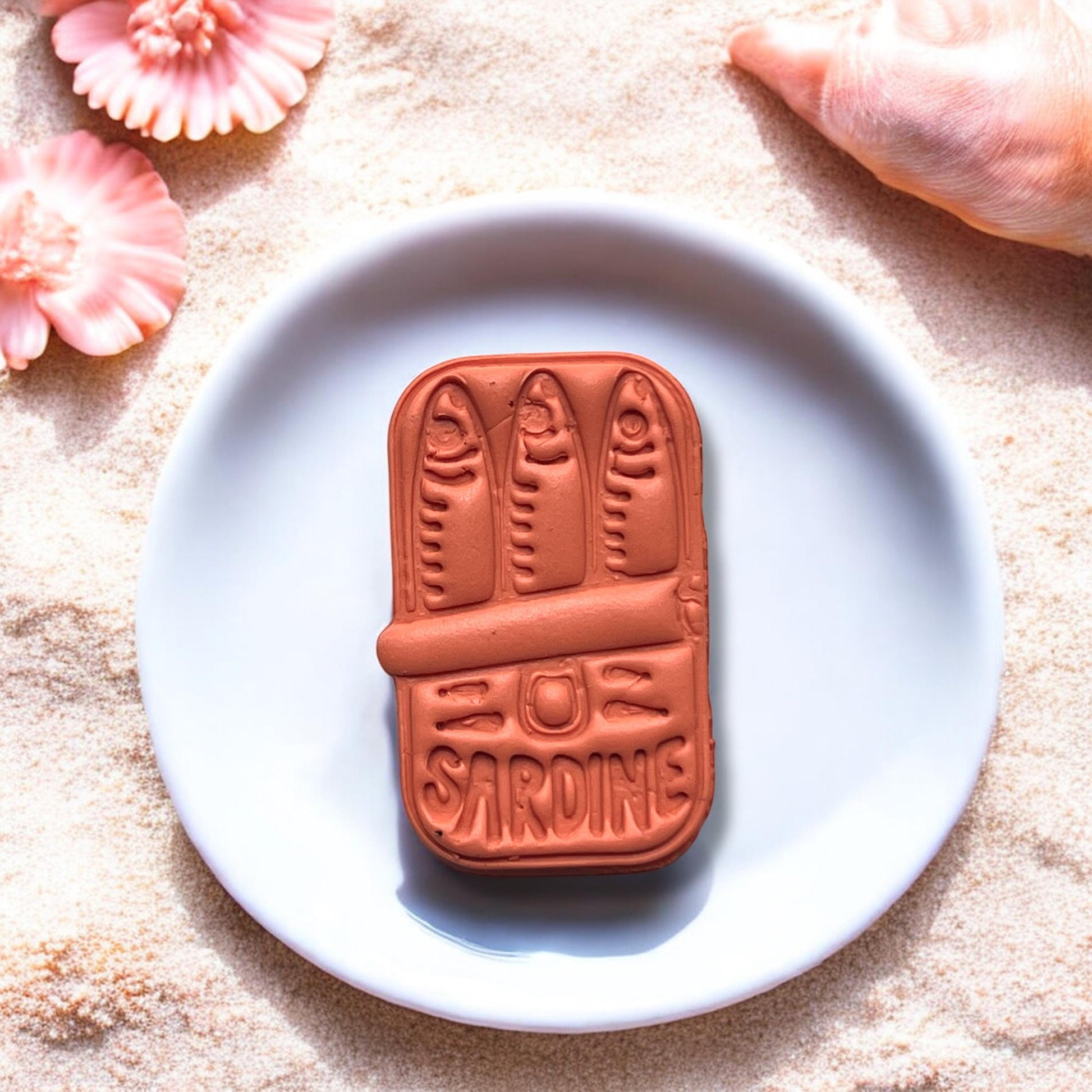 Close-up of completed sardine can clay charm on ceramic plate with beach background