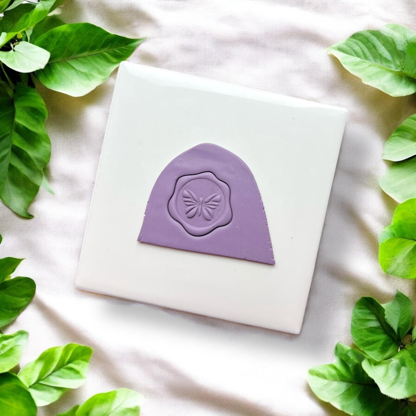 Purple clay impression with butterfly seal shape on white tile and green leaves