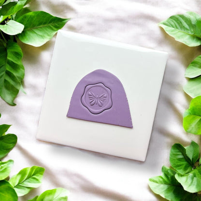 Purple clay impression with butterfly seal shape on white tile and green leaves