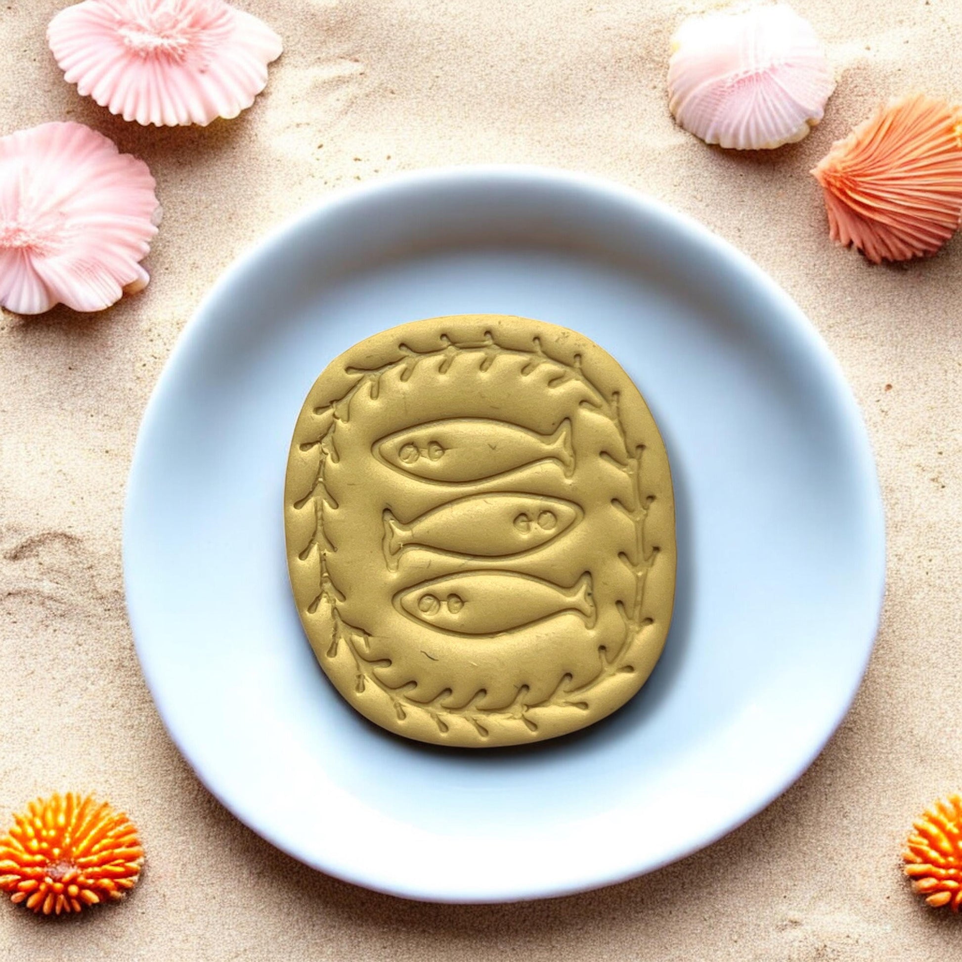 Yellow clay stamped with trio fish design on white tile and beach background
