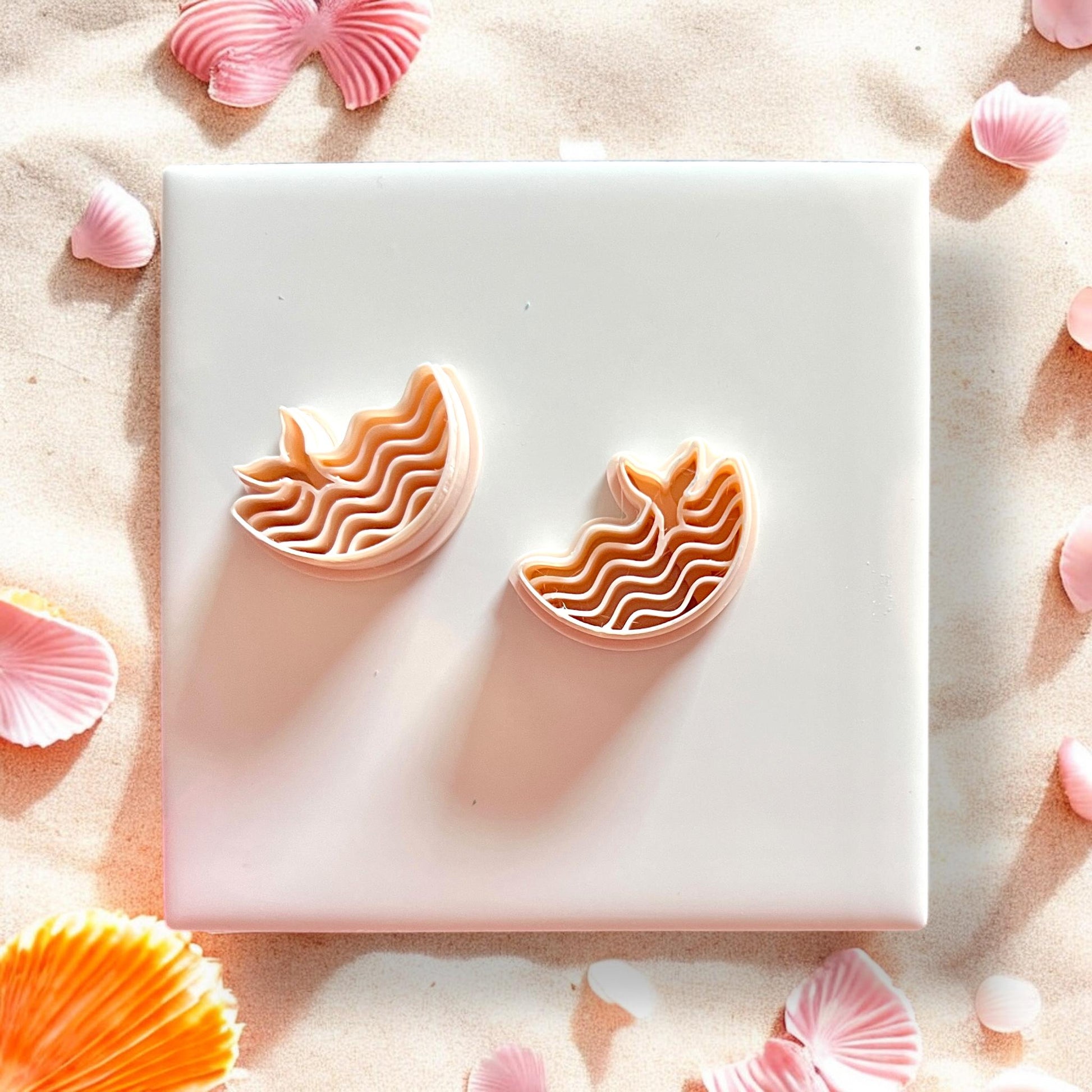 Two whale tail ocean cutters displayed on tile with shells