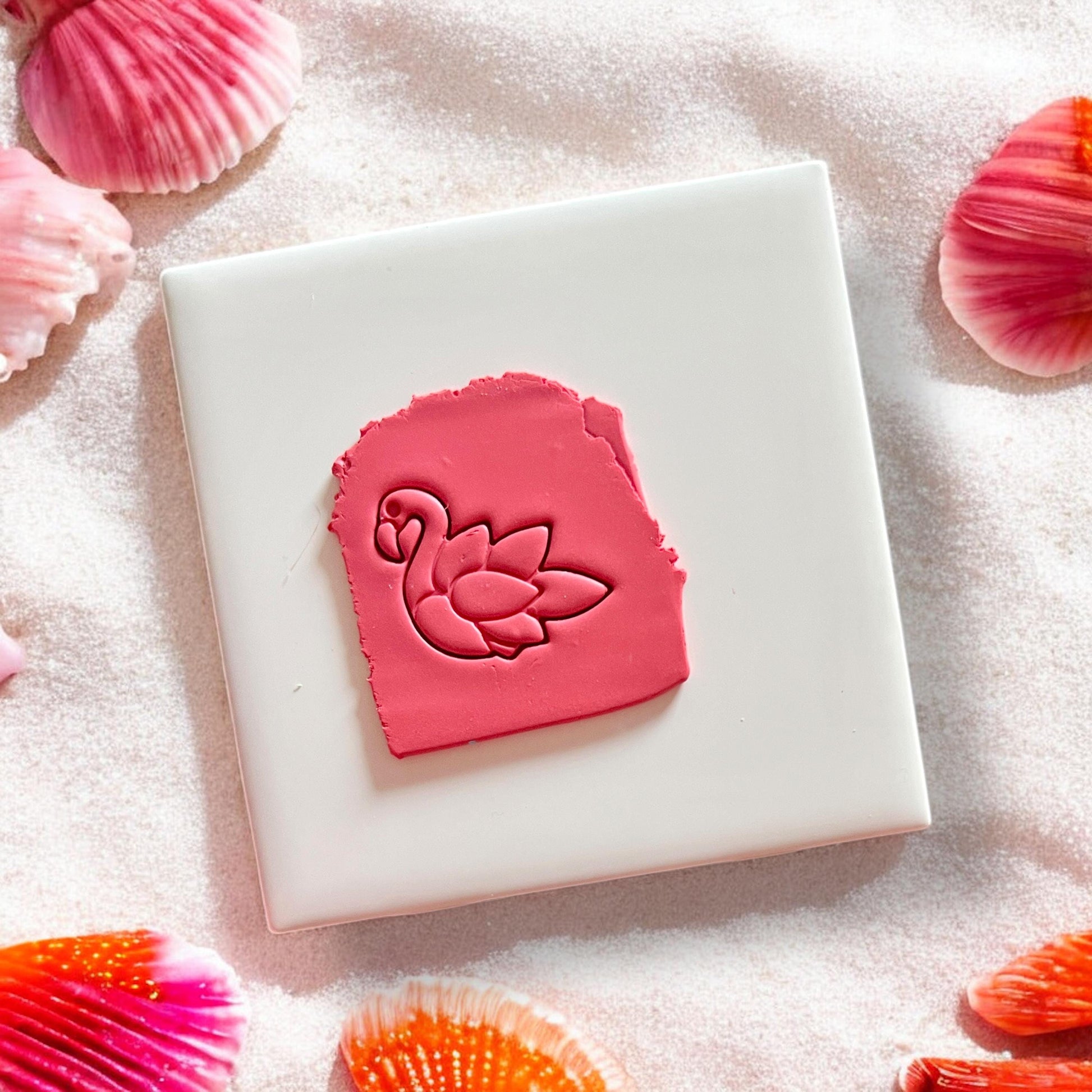Flamingo imprint in pink clay on white tile with seashell background
