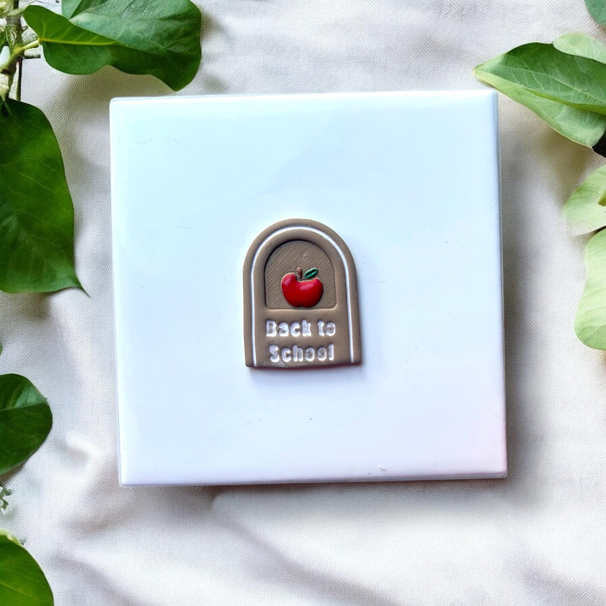 Finished clay earring with painted apple and white text