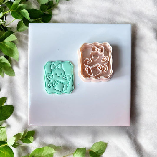 Polymer clay impressions of octopus with bow and book