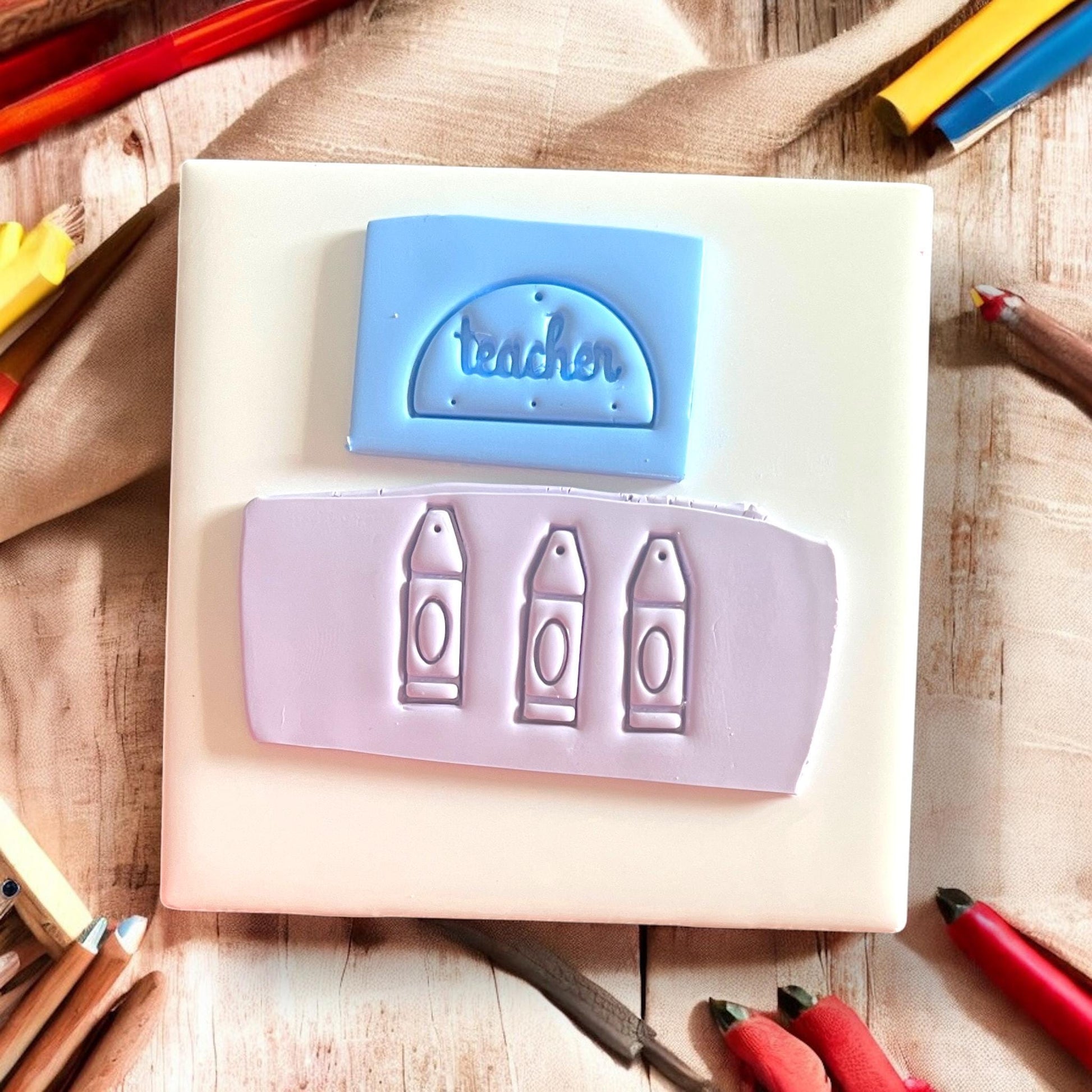 Clay slab impressions of the word “teacher” and crayon shapes