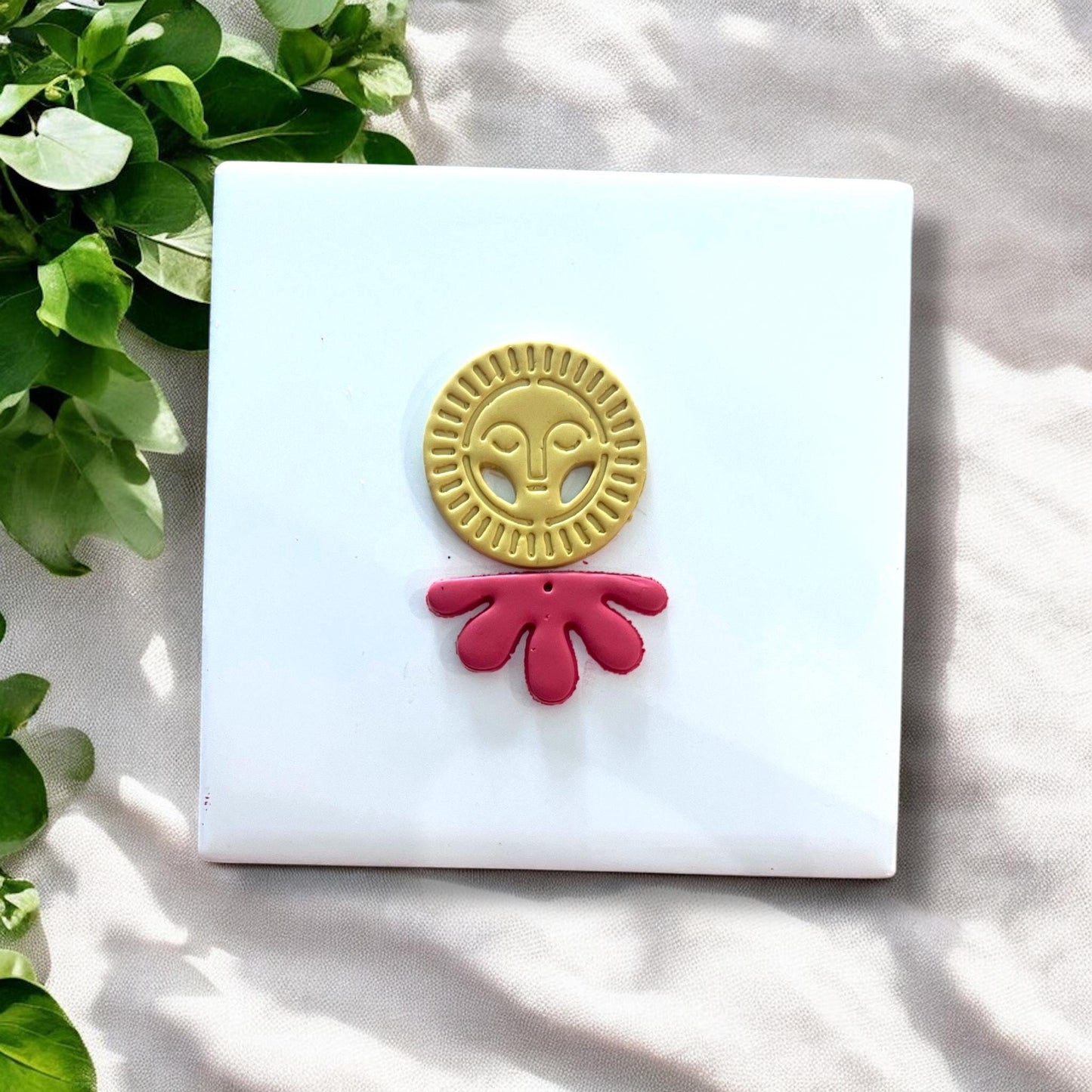 Finished yellow sun face and red flower drop clay pieces next to matching cutters