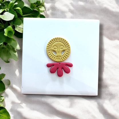 Finished yellow sun face and red flower drop clay pieces next to matching cutters