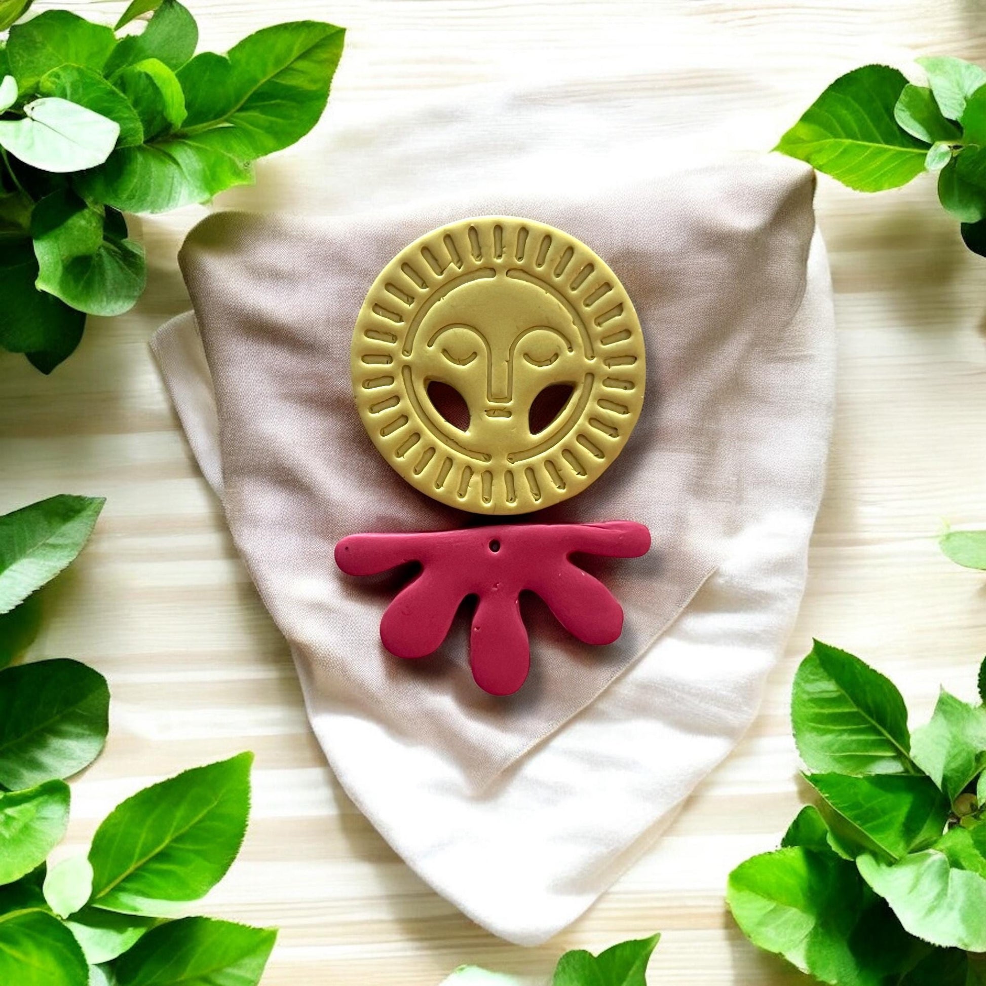 Close-up of full earring design: yellow radiant sun face and red drop accen