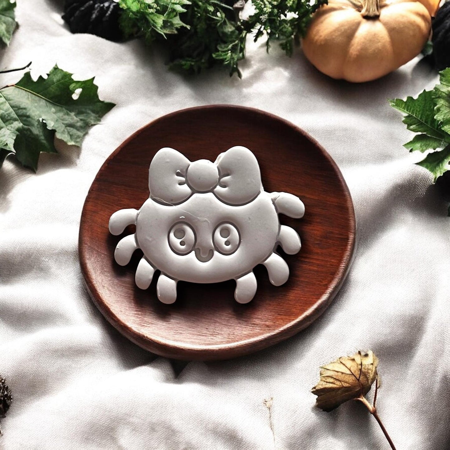 Clay spider with bow on round wooden plate