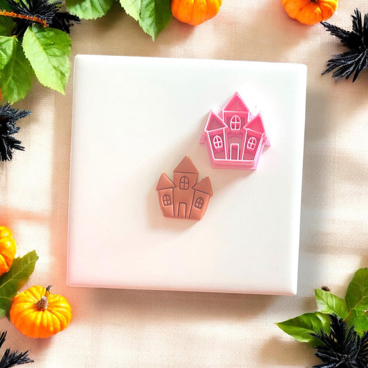Orange clay cutout of haunted house next to pink plastic cutter