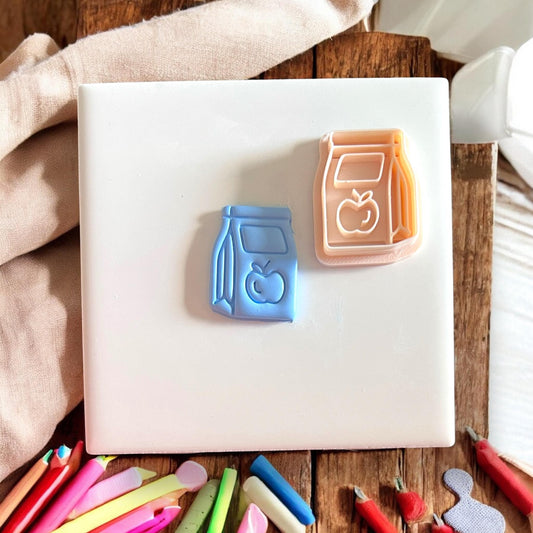 lunch bag and apple clay impression with matching cutter on white tile