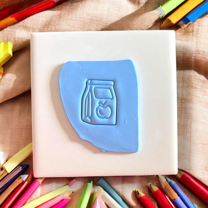 blue clay impression of a lunch bag and apple design