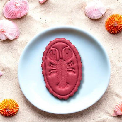 Large completed lobster oval charm displayed on plate with beach decor