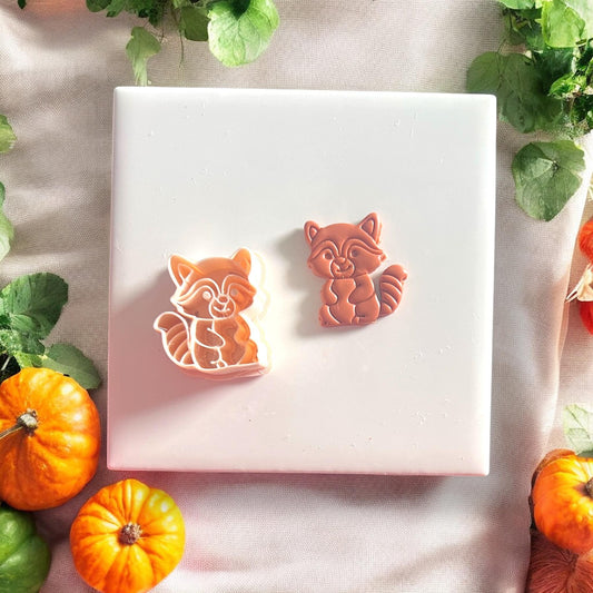Halloween raccoon polymer clay cutter and finished piece side by side on display tile