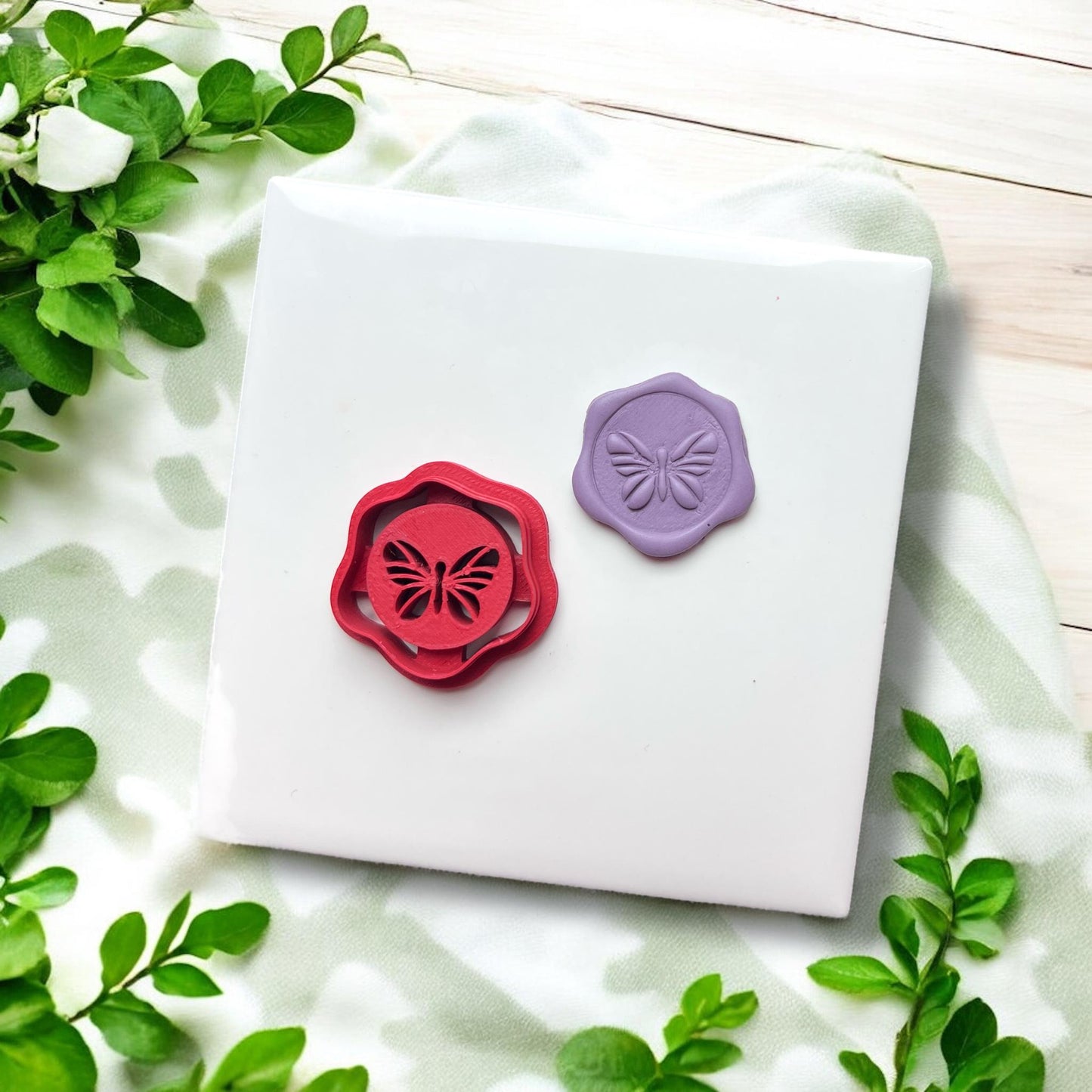 Side-by-side red cutter and purple butterfly stamped piece on tile