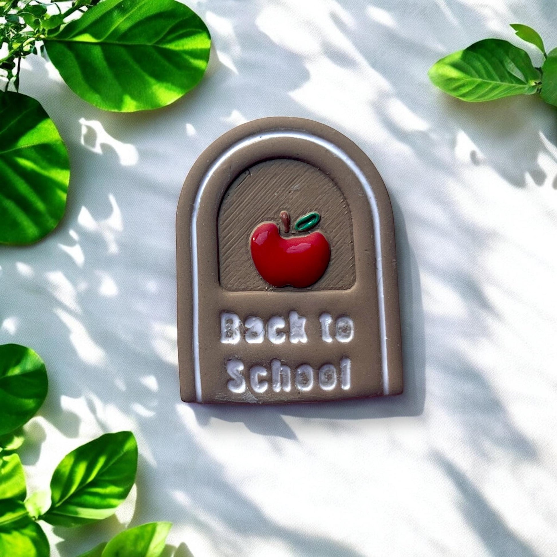 Finished clay earring with painted apple and white text