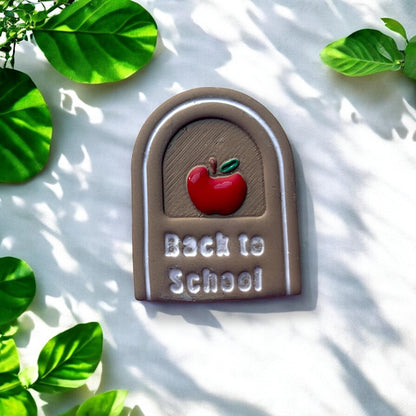 Finished clay earring with painted apple and white text