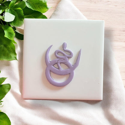 Finished snake pendant cut from clay, laid on white square tile