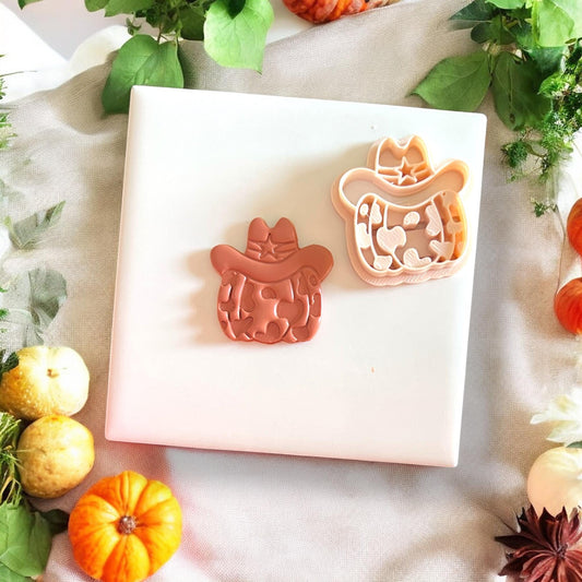 Polymer clay cutter in cowprint pumpkin shape with hat, placed on white tile