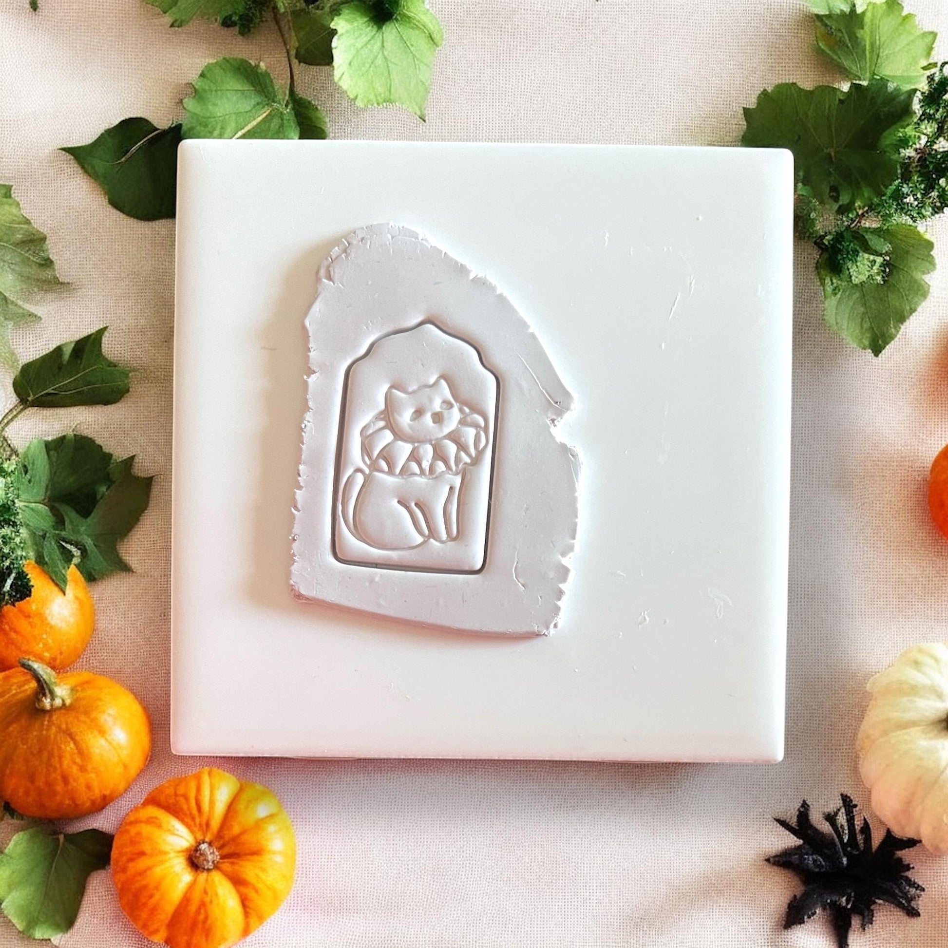 Clay slab with Halloween cat wearing jester collar, surrounded by fall leaves