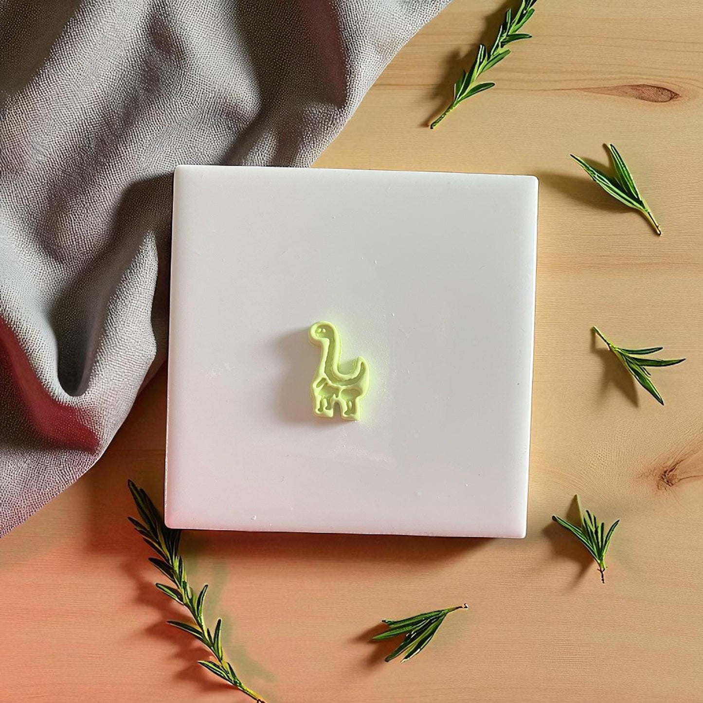 Finished clay dino shape displayed with neutral fabric and herbs