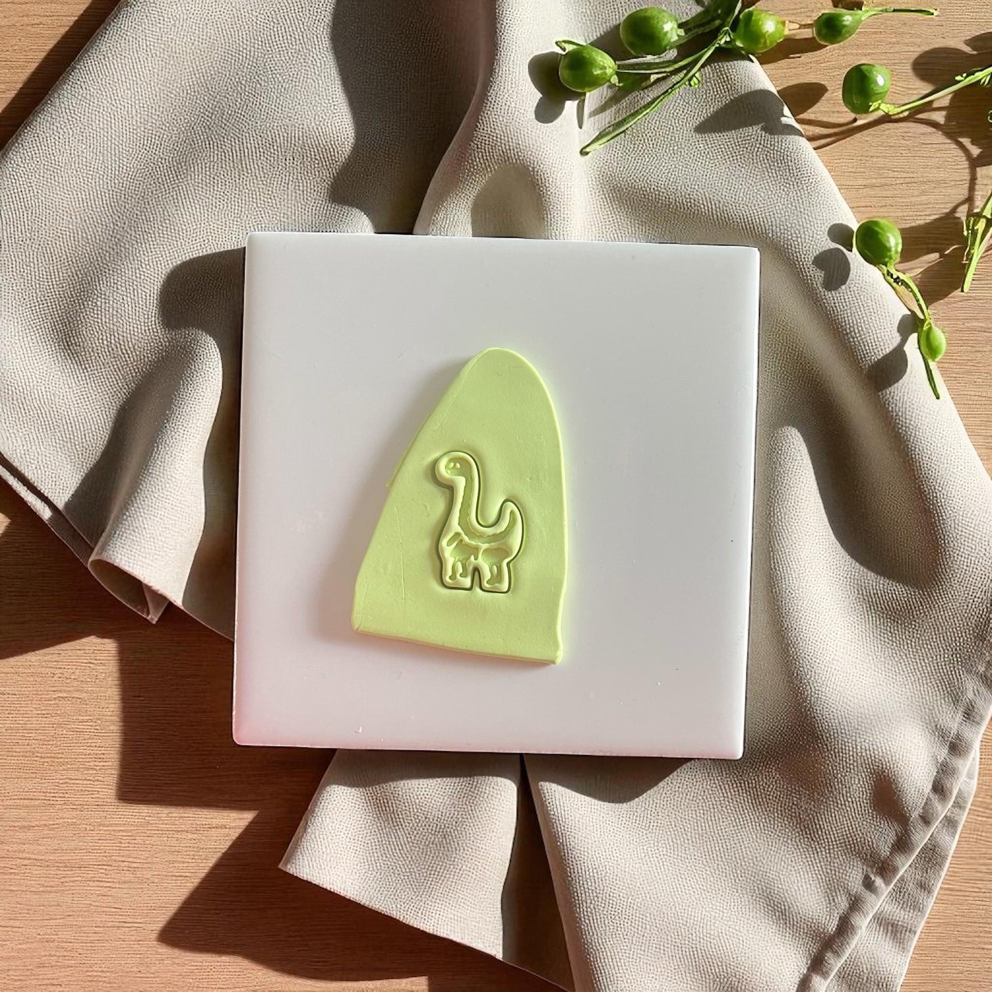 Polymer clay imprint of dinosaur cutter with curved tail and leaf props