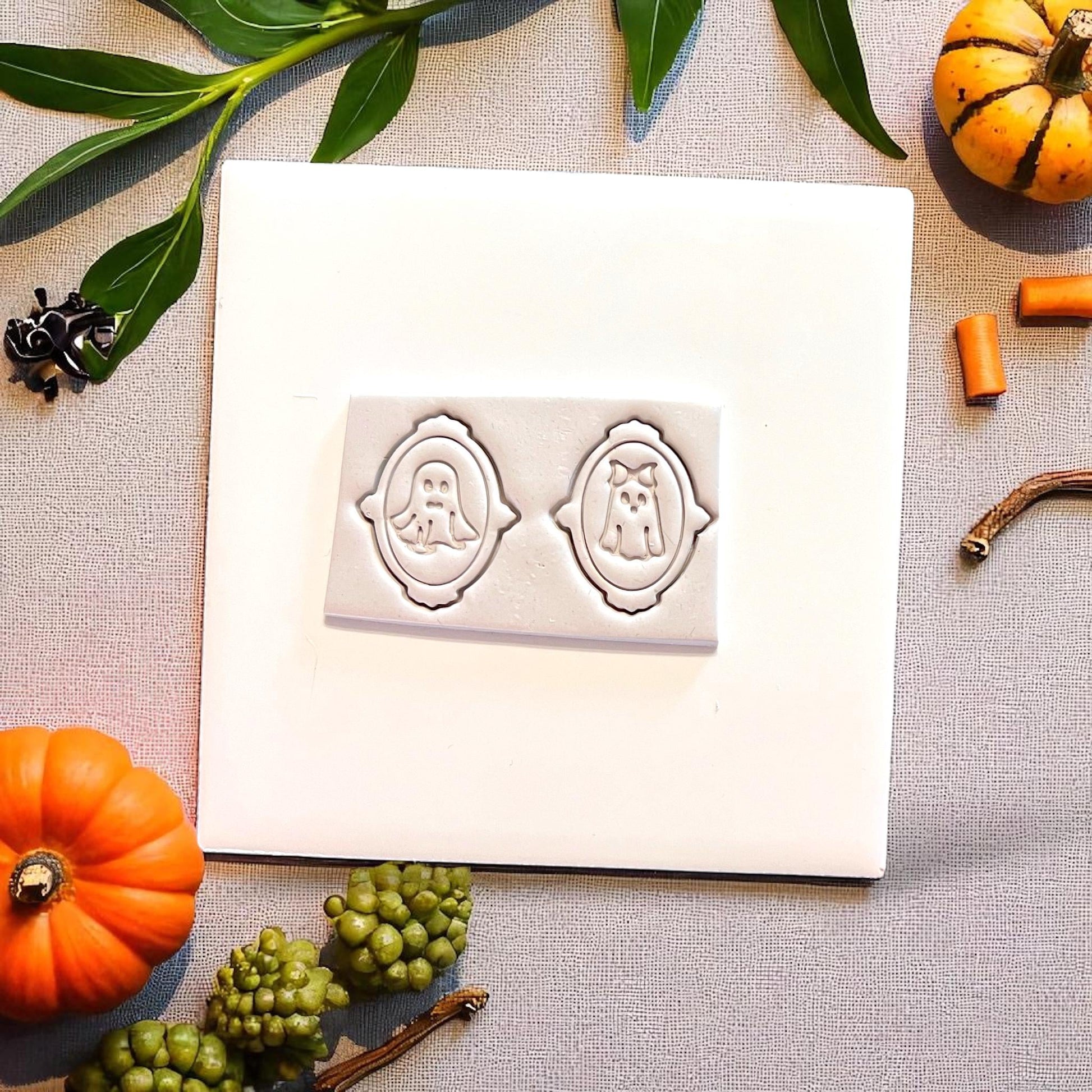 Mr. and Mrs. ghost cutters pressed in clay on white tile with pumpkins and greenery