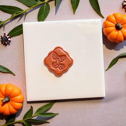 Pumpkin cherry clay cutout centered on a square tile with pumpkins and greenery