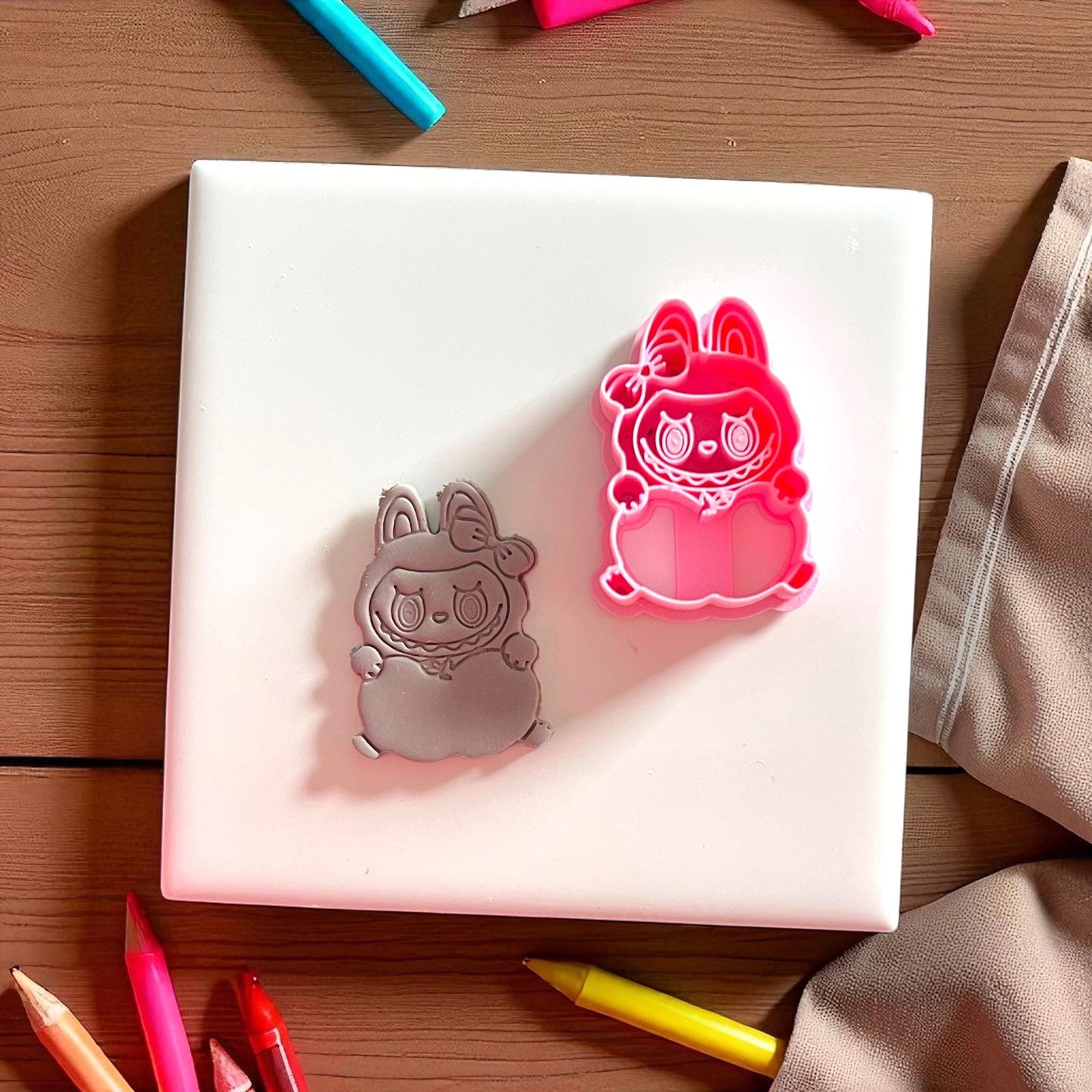 Apple holding monster clay imprint beside pink cutter on white tile