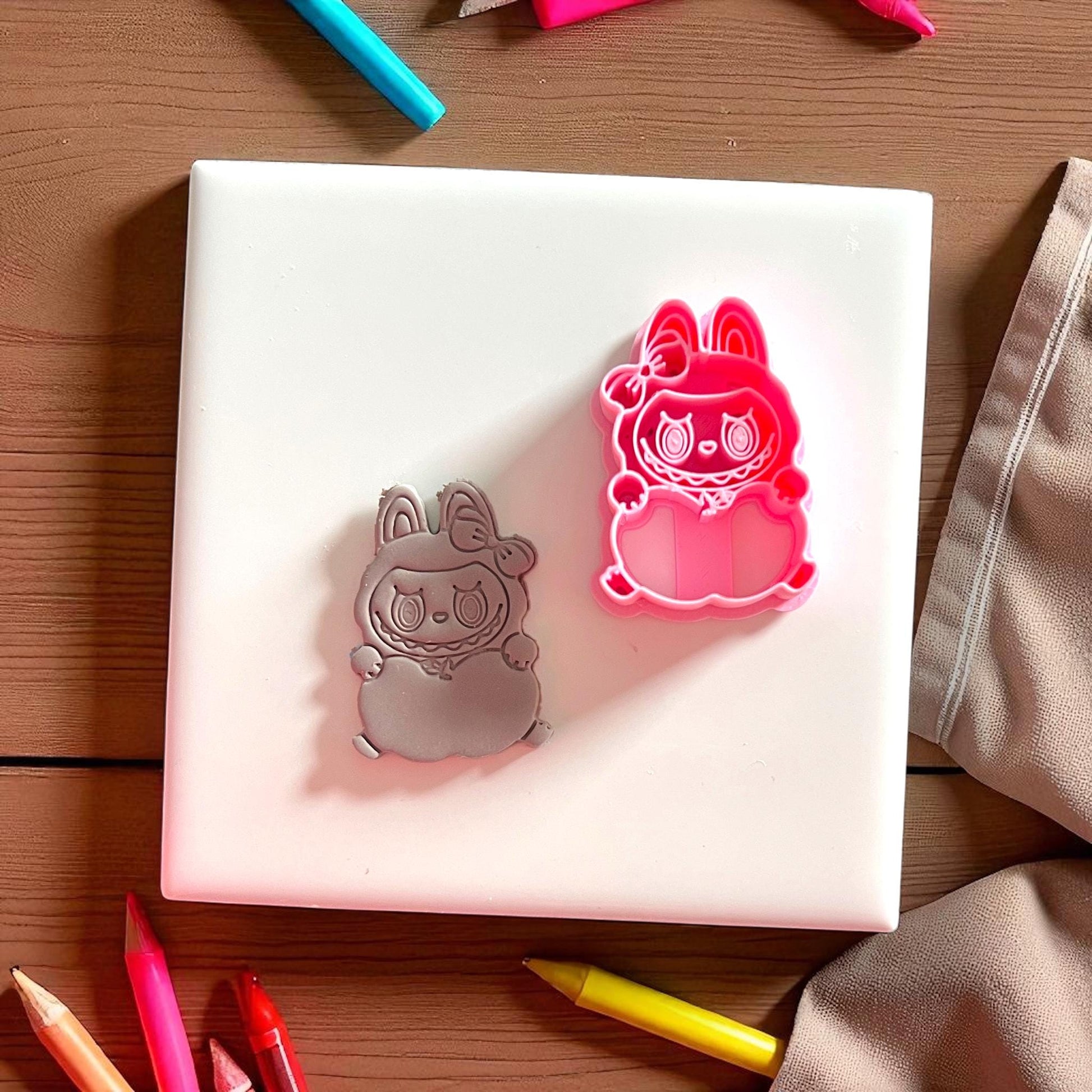 Apple holding monster clay imprint beside pink cutter on white tile