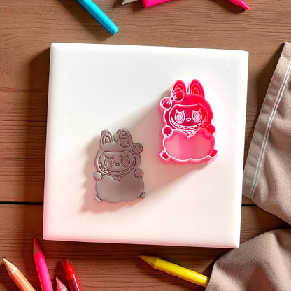 Apple holding monster clay imprint beside pink cutter on white tile