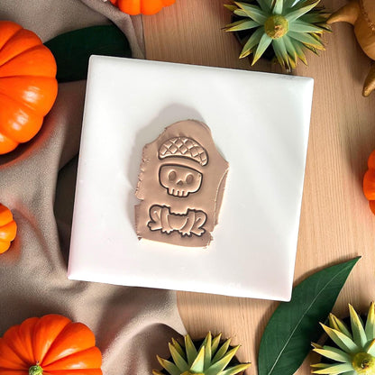 Skull frog clay impression with acorn hat on white tile and pumpkins