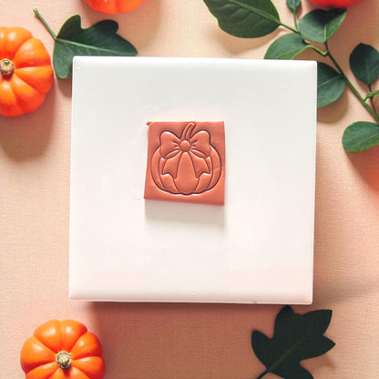 Pumpkin with bow clay earring on white tile