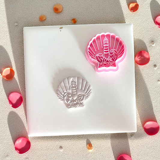 Pink polymer clay cutter with lighthouse in shell shape, next to impressed slab