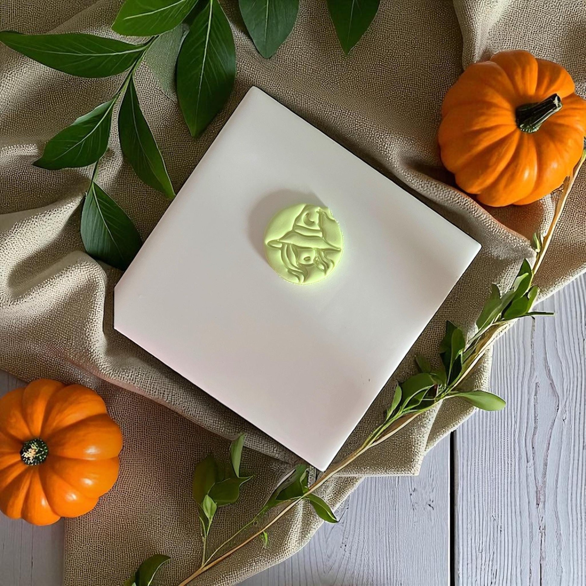 Sexy witch polymer clay imprint centered on white tile with pumpkins and greenery