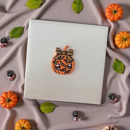 Clay pumpkin with bow and bat design on display tile with mini pumpkins