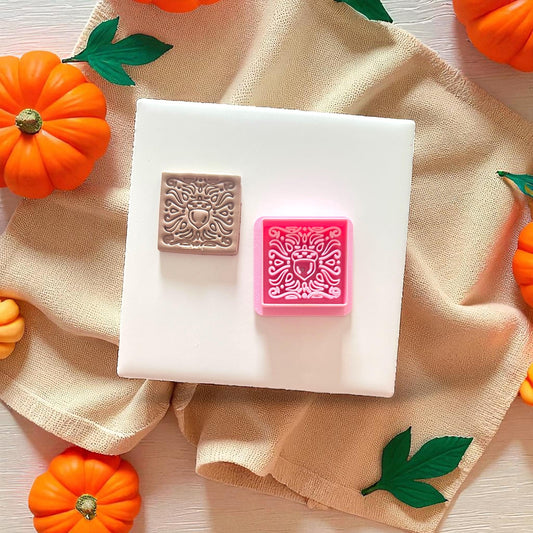 Clay imprint next to pink acorn cutter on fabric backdrop with pumpkins