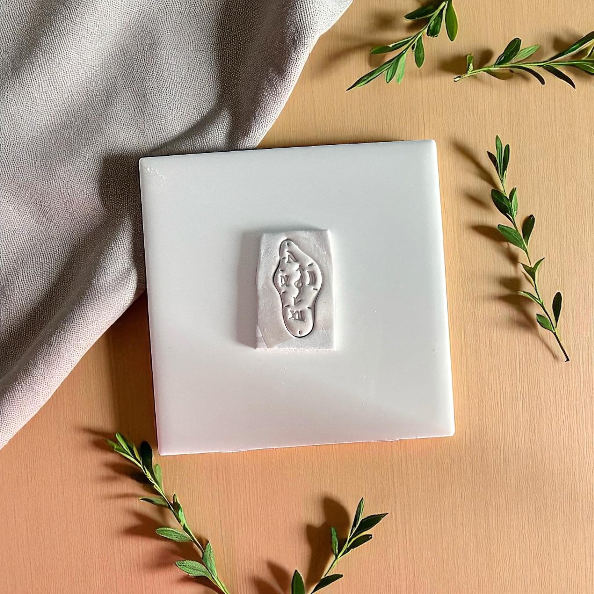 melting clock polymer clay cutter on square tile with greenery