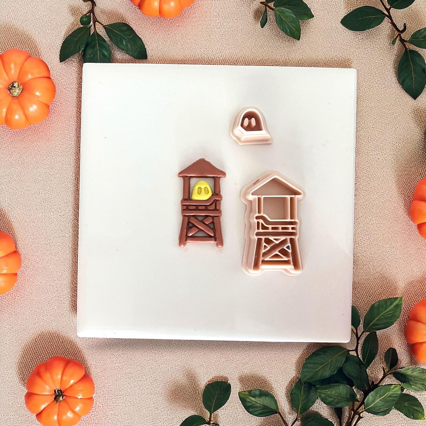 Finished ghost lifeguard tower clay piece on a white plate with greenery and pumpkins.