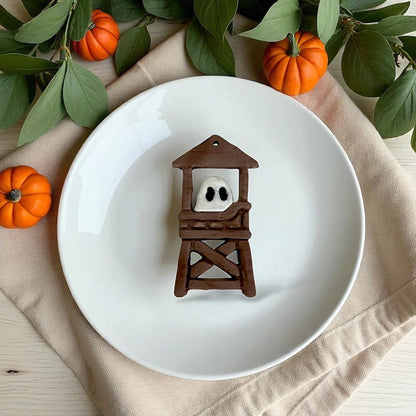 Close-up of finished ghost lifeguard tower charm on white plate with leaves and pumpkins.