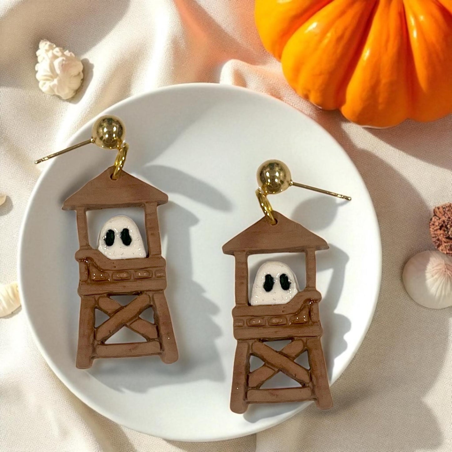 Pair of ghost lifeguard tower earrings with gold posts styled with pumpkin and seashells.