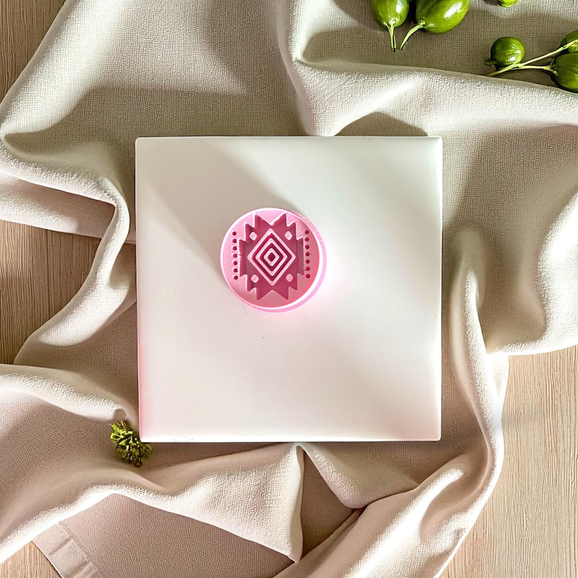 Pink round geometric clay cutter with diamond tribal motif displayed on white square tile and neutral fabric.