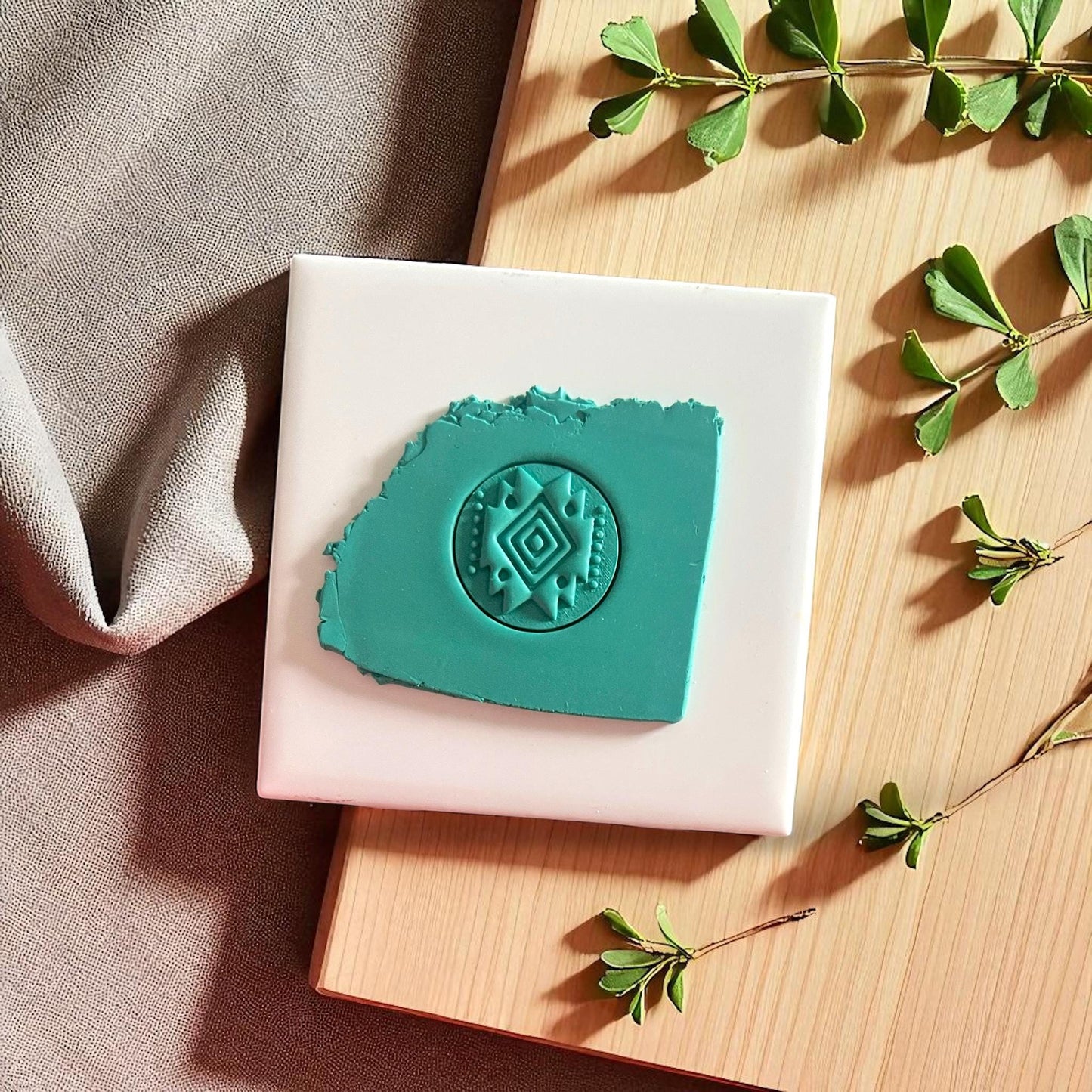 Teal clay imprint of round tribal diamond cutter pressed into clay, displayed on white tile and wooden board.