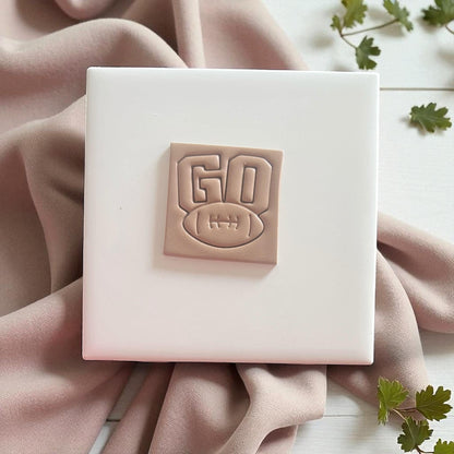 GO football polymer clay earring design on blush fabric backdrop