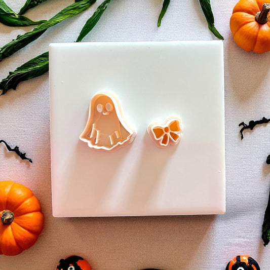 Polymer clay cutters shaped like a ghost and bow on white tile