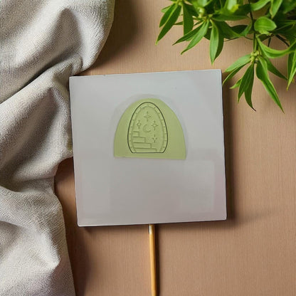 Green arched clay imprint with staircase, moon, and stars on white tile and fabric background.
